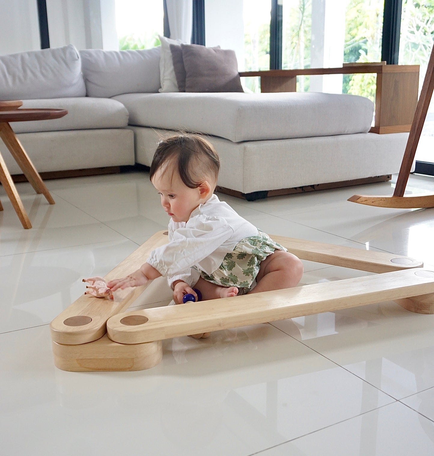 Baby playing with a Dahan Balance Beams on a tiled floor in a modern living room.