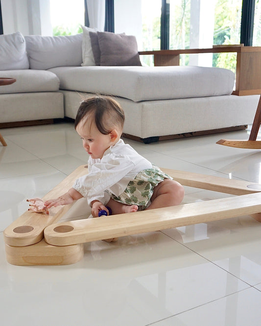 Baby playing with a Dahan Balance Beams on a tiled floor in a modern living room.